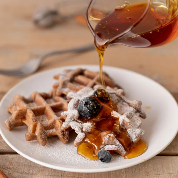 Une assiette de gaufres avec du sirop versé dessus, garnie de fruits frais.