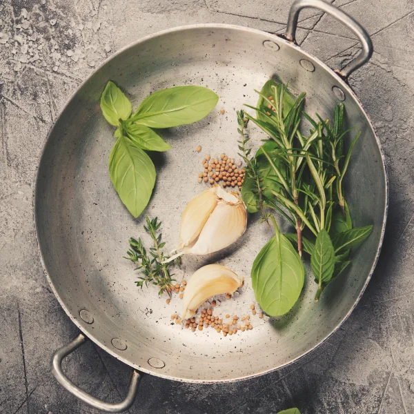Herbes fraîches et ail dans une poêle, prêts à être cuisinés pour rehausser les saveurs des plats.