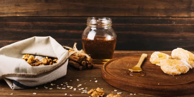 Une table en bois avec un pot de miel, des noix et un sachet de biscuits, créant un mélange savoureux.